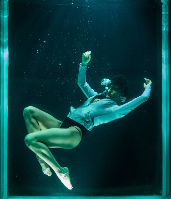 Woman performing a fluid cardio movement in a dark studio with cyan light trails.